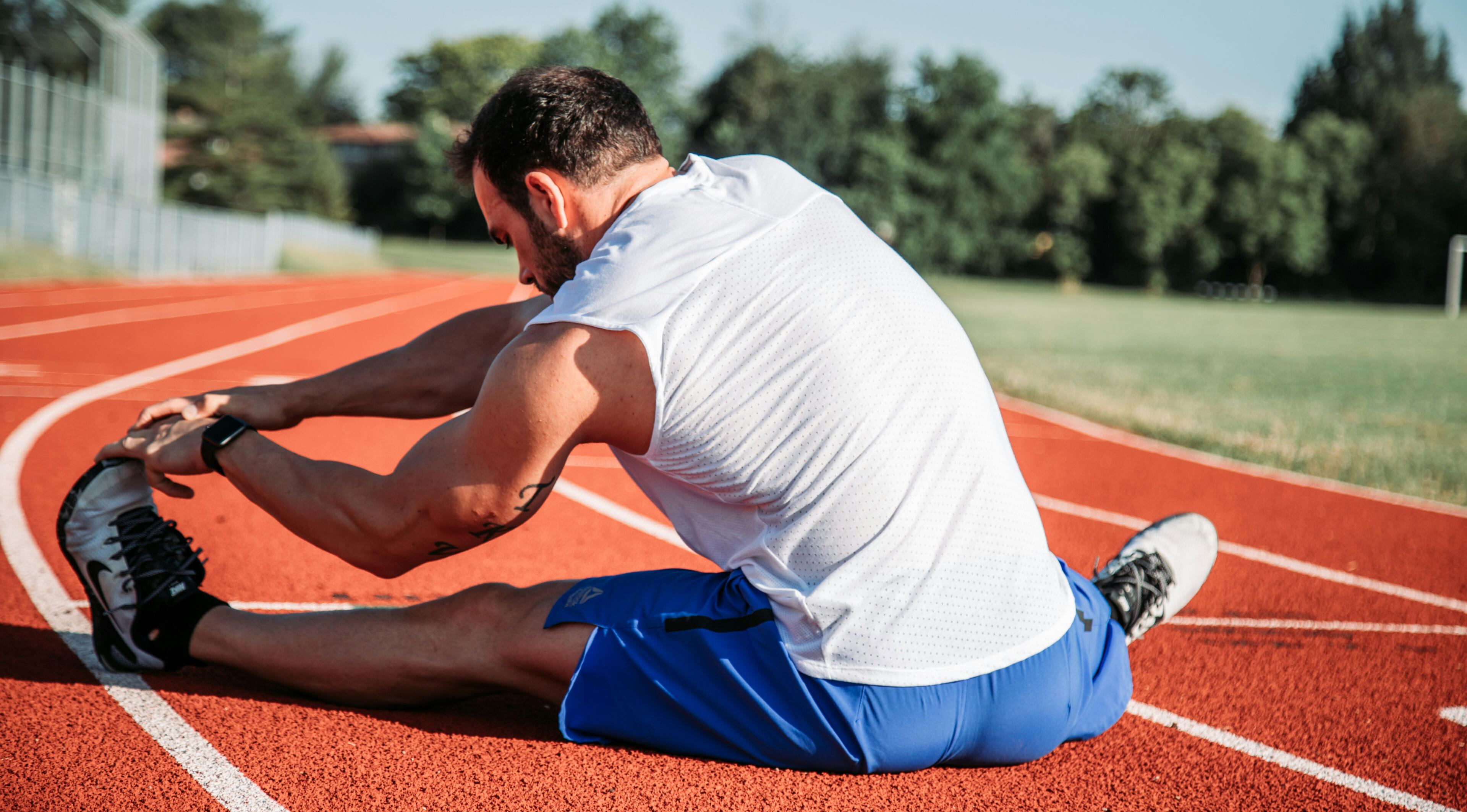 A person doing a seated hurdlers stretch on a track field, increasing his flexibility.